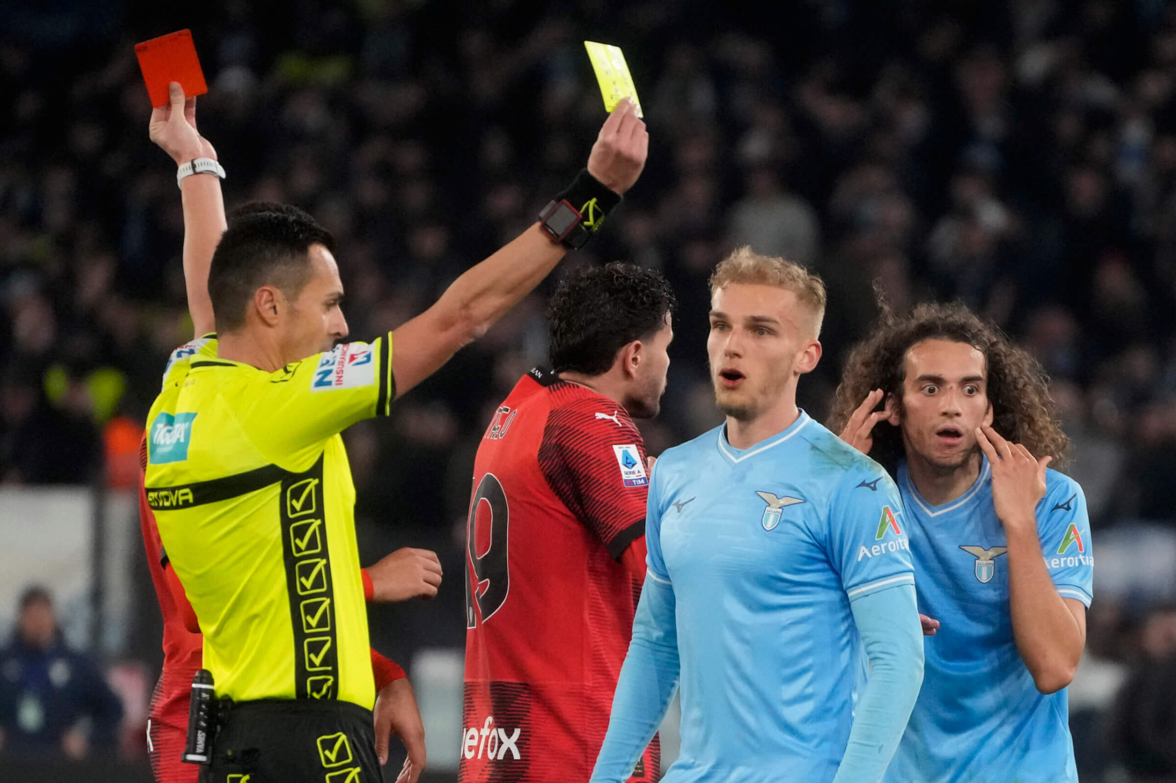 Referee Marco di Bello shows the red card to Lazio's Matteo Guendouzi, background right, and the yellow card to AC Milan's Christian Pulisic during the Italian Serie A soccer match between Lazio and Milan at Rome's Olympic stadium, Friday, March 1, 2024. (AP Photo/Gregorio Borgia)